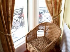 Ein Korbstuhl an einem Fenster mit Blick auf einen Balkon.