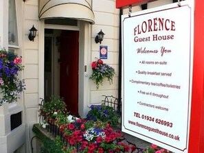 Placa da Florence Guest House, indicando comodidades como quartos privativos, café da manhã, chá/café/produtos de higiene pessoal gratuitos, Wi-Fi grátis e recepção de prestadores de serviços.