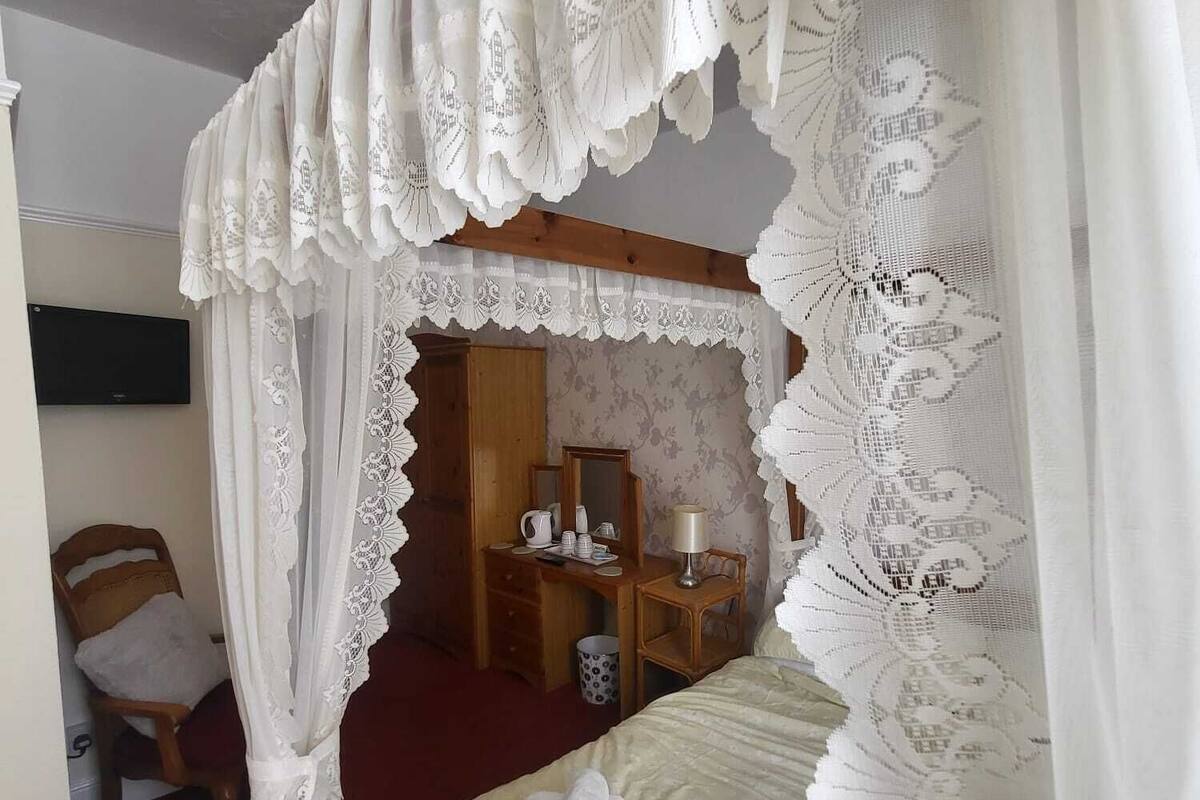 A bedroom with a four-poster bed, a wooden desk, and a chair.