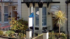 Un bâtiment traditionnel doté d’un balcon, d’un petit jardin et d’une plante particulière, reconnaissable à ses feuilles pointues.