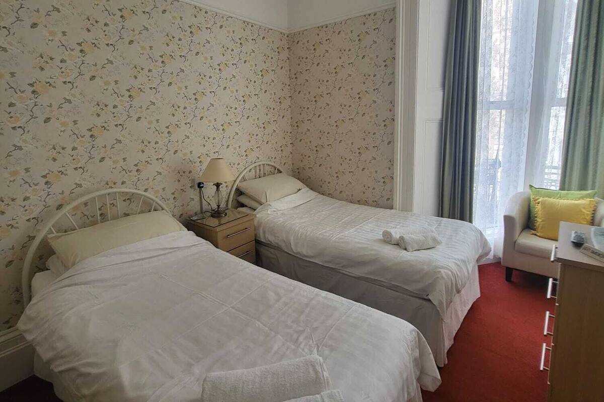 A hotel room with two beds, a desk, a chair, and a window with curtains.