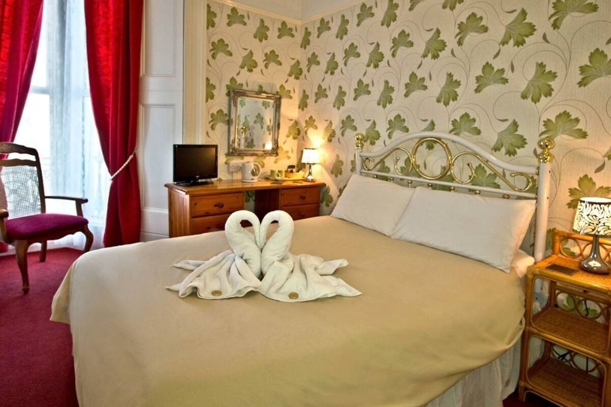 A hotel room with a bed, a television, a desk with a lamp, and a chair.