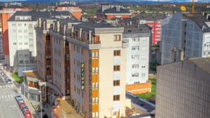 A multi-story hotel with a central courtyard, a parking lot, and a view of the surrounding cityscape. - Hostal Bríos (Lugo)