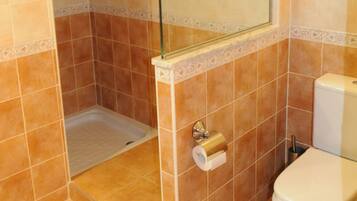 Un baño con cabina de ducha de vidrio, inodoro y un rollo de papel higiénico en la pared.
