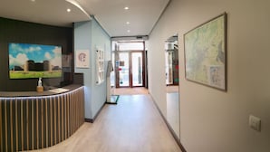 A hotel reception area with a curved reception desk, a large painting of a landscape, a map on the wall, and a view into the lobby. - Hostal Bríos (Lugo)