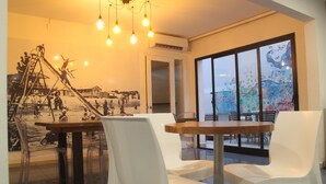 A dining area with a wooden table and white chairs, a mural on the wall, and a view through large windows. - Hotel Florinda (Punta del Este)