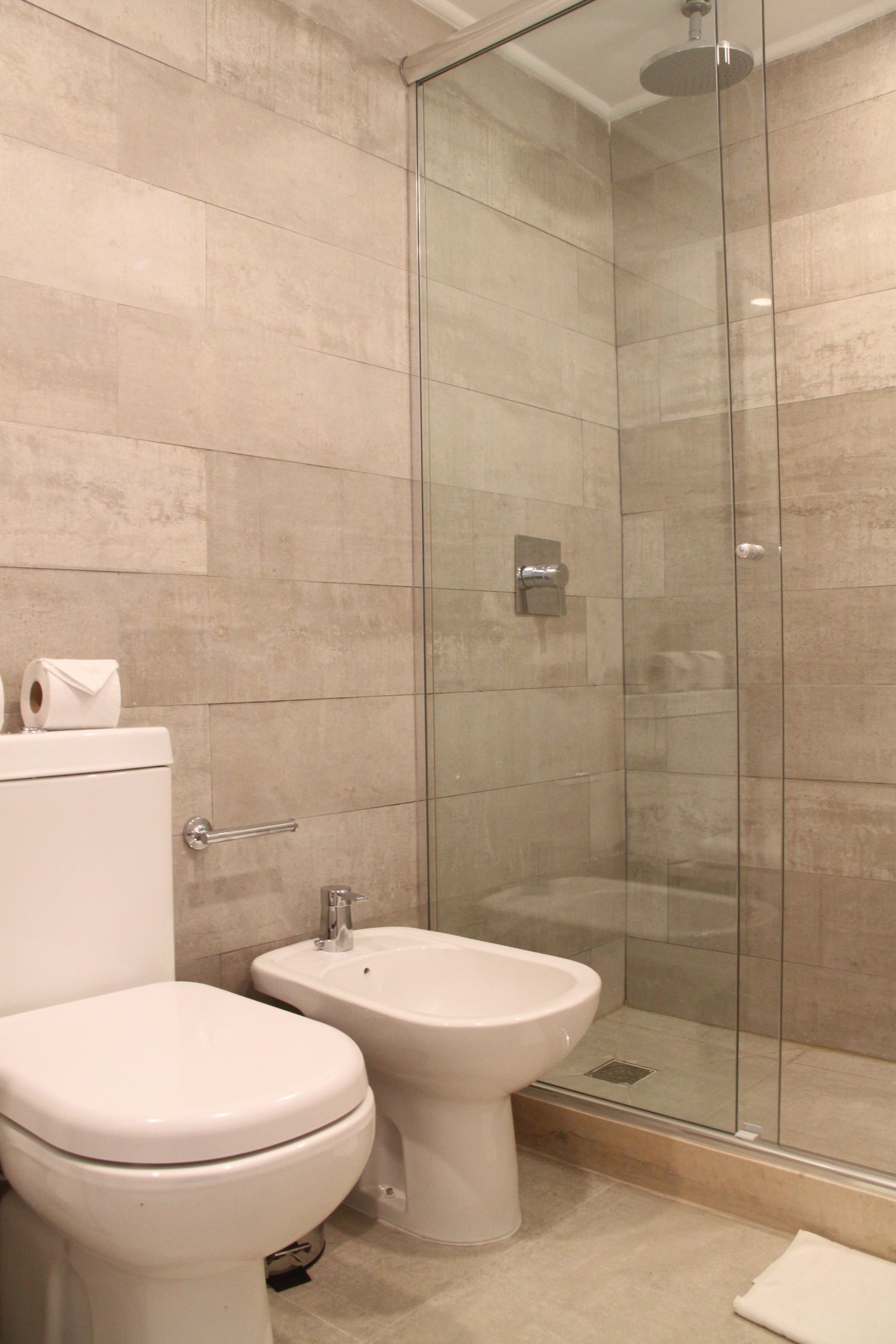 Un baño moderno con inodoro, bidé y ducha con mampara de vidrio.