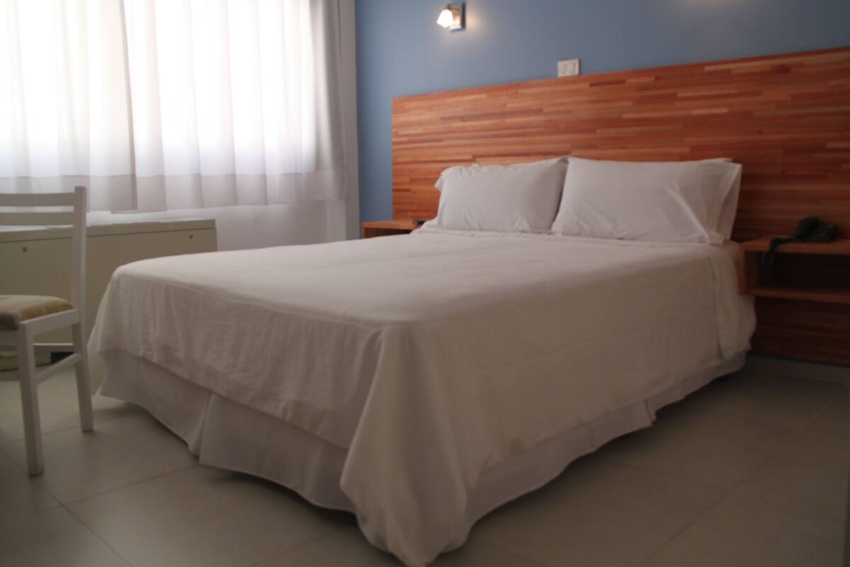 A neatly made bed with a wooden headboard, a bedside table with a lamp, and a chair.