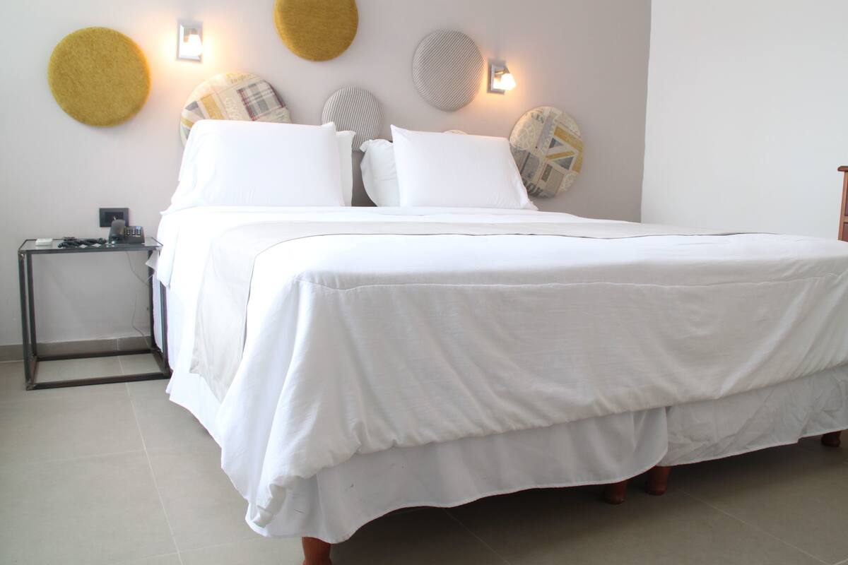 A neatly made bed with white bedding, a bedside table with a lamp, and decorative wall art.