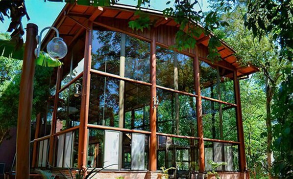 A wooden structure with large windows, surrounded by trees.