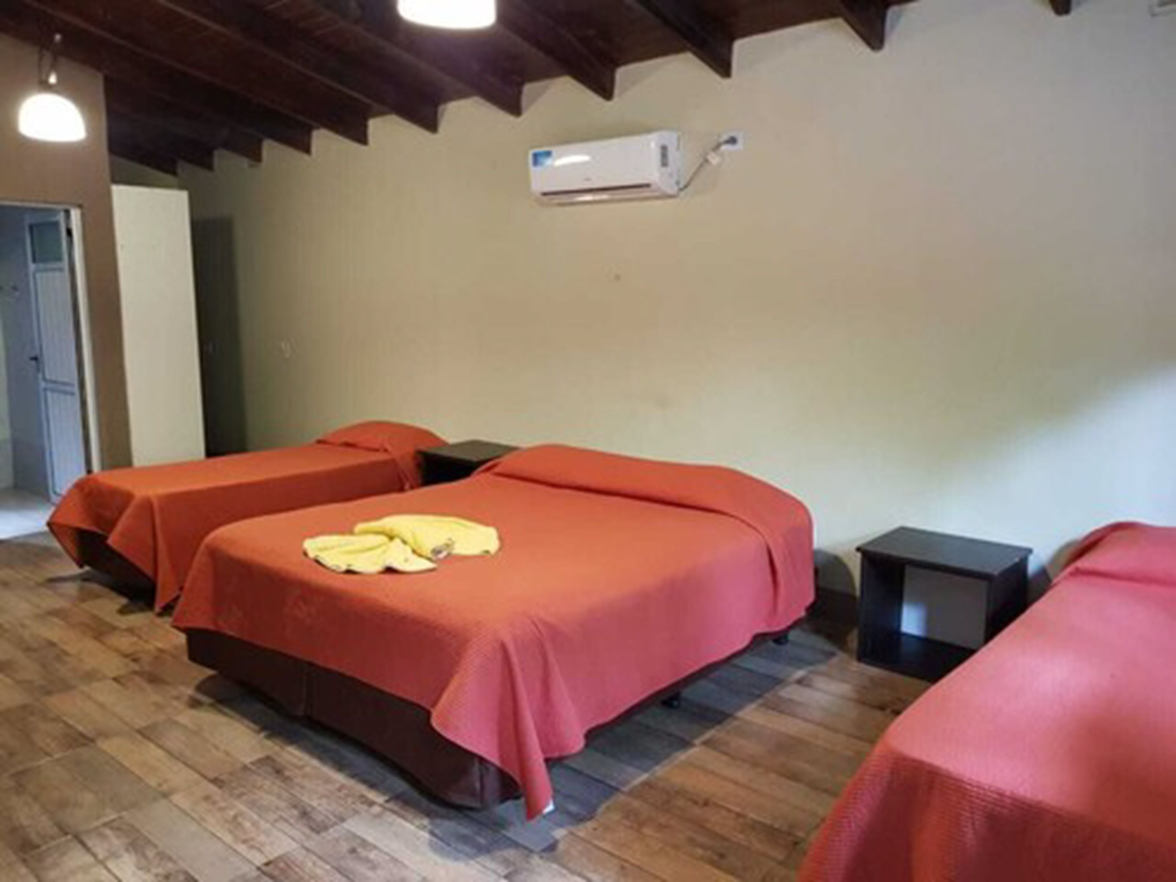 Ein Zimmer mit zwei Betten, jedes mit einer roten Decke, und einem kleinen Tisch neben einem Bett.