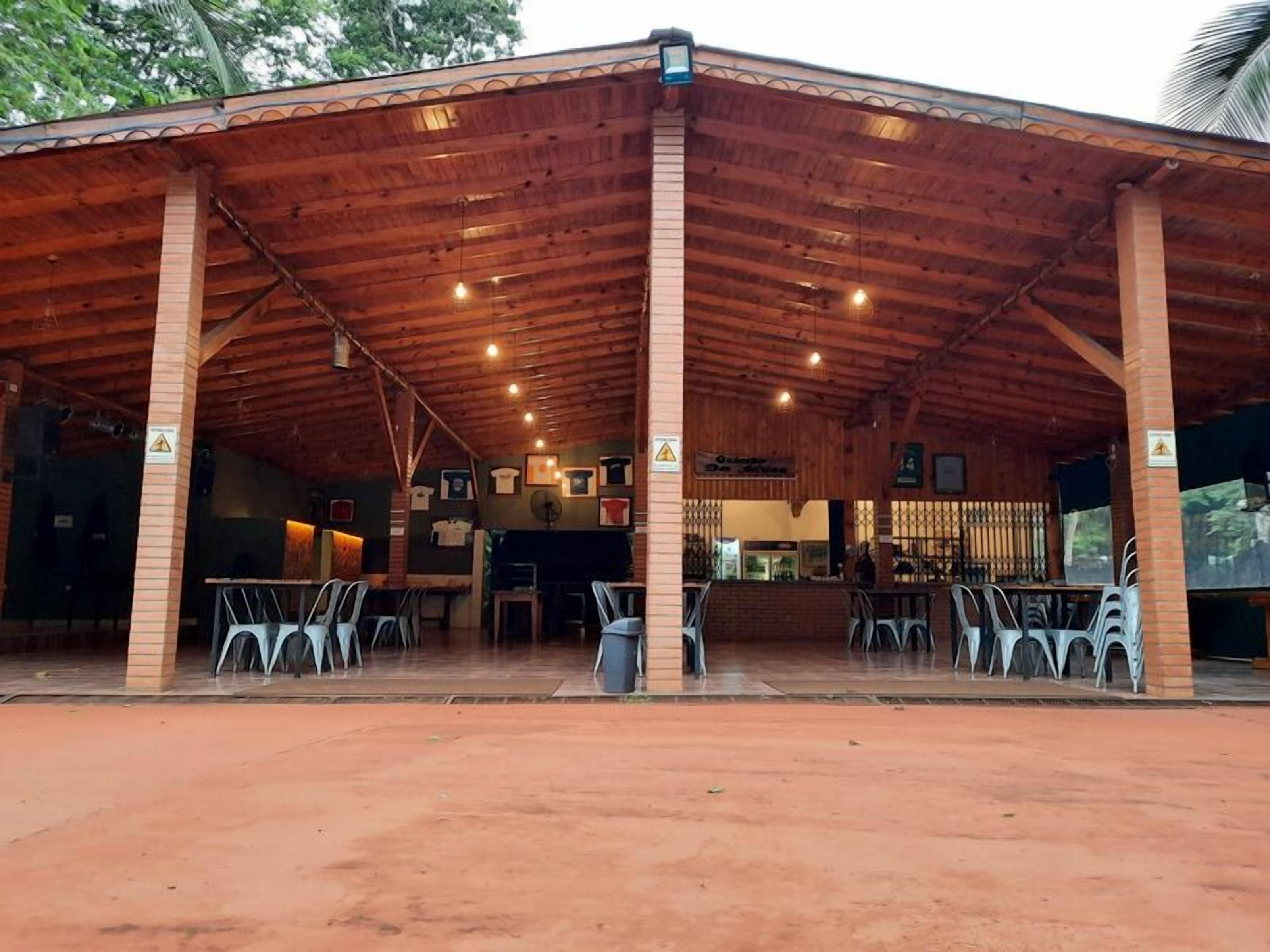A covered outdoor seating area with tables and chairs, a brick wall, and a sign indicating a restaurant or cafe.