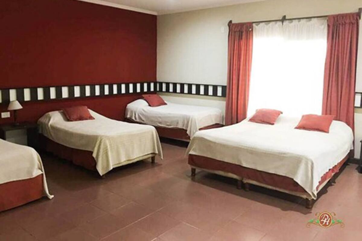 Une chambre d’hôtel avec quatre lits simples, un mur d’accent rouge, une fenêtre avec des rideaux rouges et un sol carrelé.