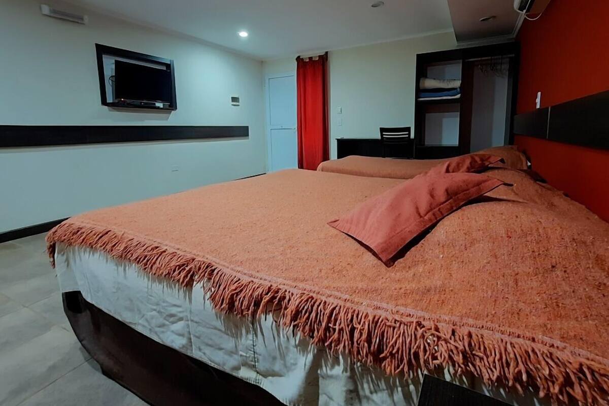 Une chambre d’hôtel avec un lit, un téléviseur fixé au mur, une armoire et un rideau rouge.