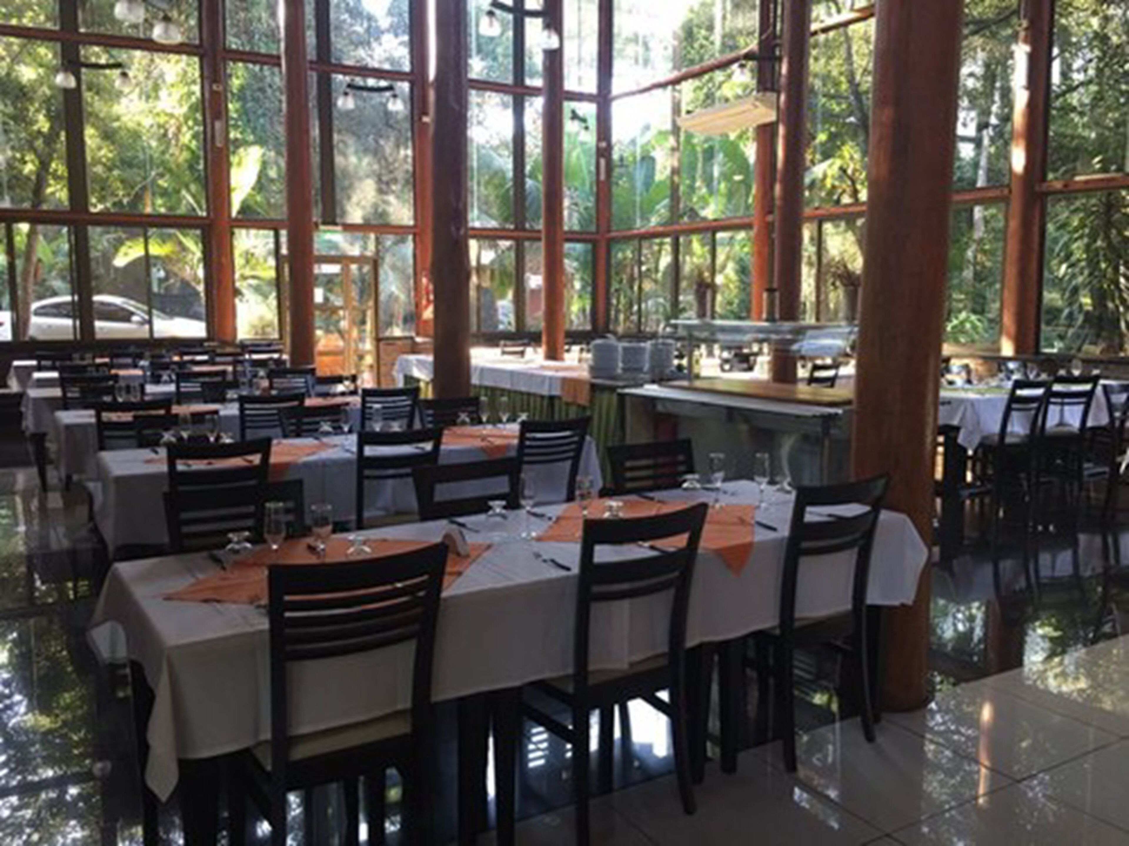 Un ristorante con diversi tavoli e sedie, ampie finestre e vista su spazi verdi.