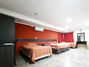 Une chambre d’hôtel avec deux lits, un mur rouge, un plafond blanc et un petit bureau avec un miroir.