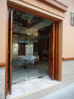 Entrada de hotel con puerta de cristal, un candelabro y un interior visible que incluye una cama y un sofá.