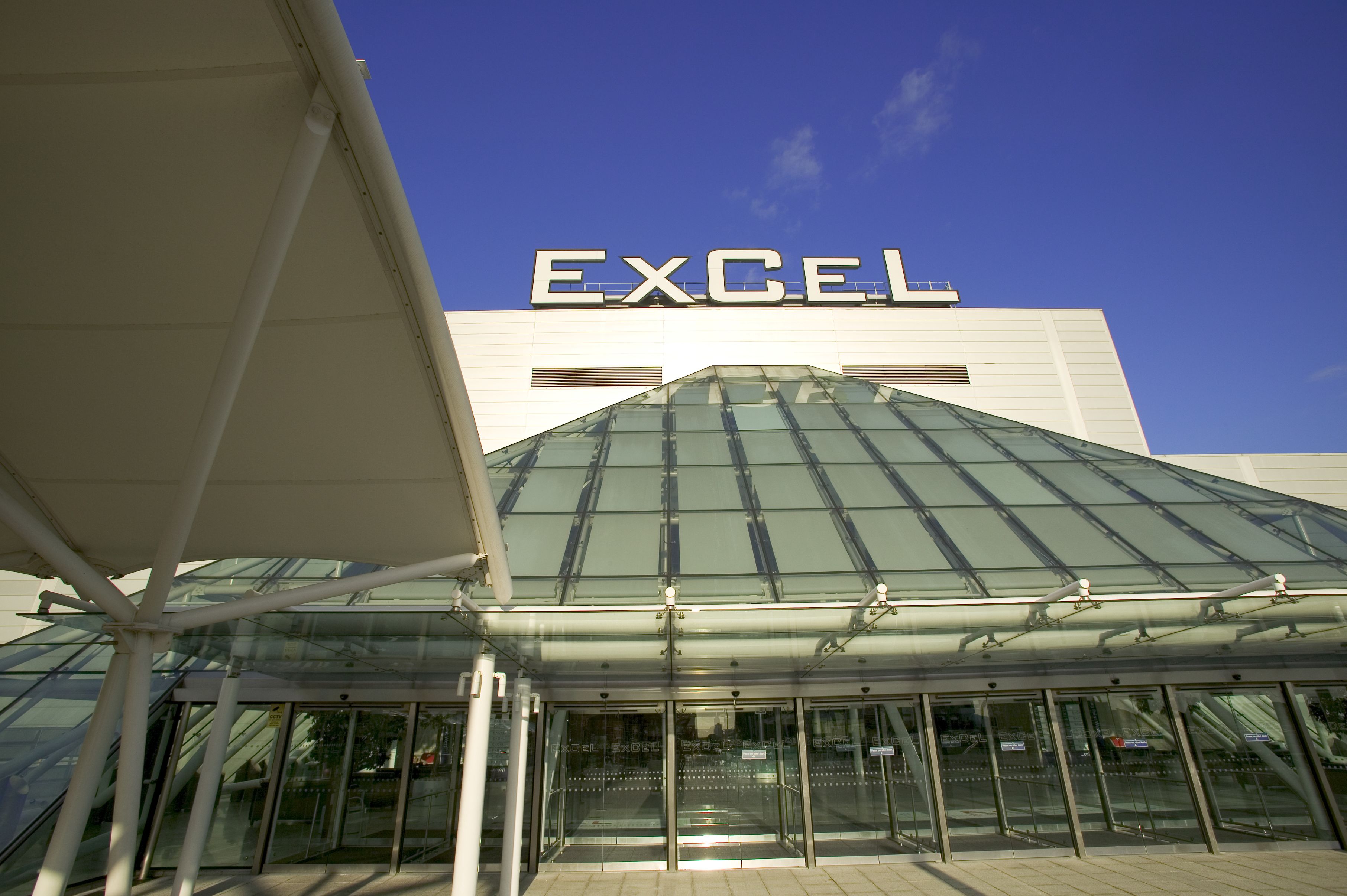 A modern building with a large "EXCEL" sign, featuring a glass entrance and a covered area with a white roof.