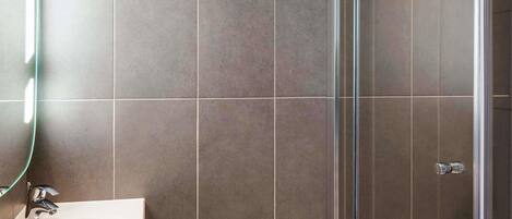 A modern bathroom with a glass shower enclosure, a white sink, and a mirror with a light.