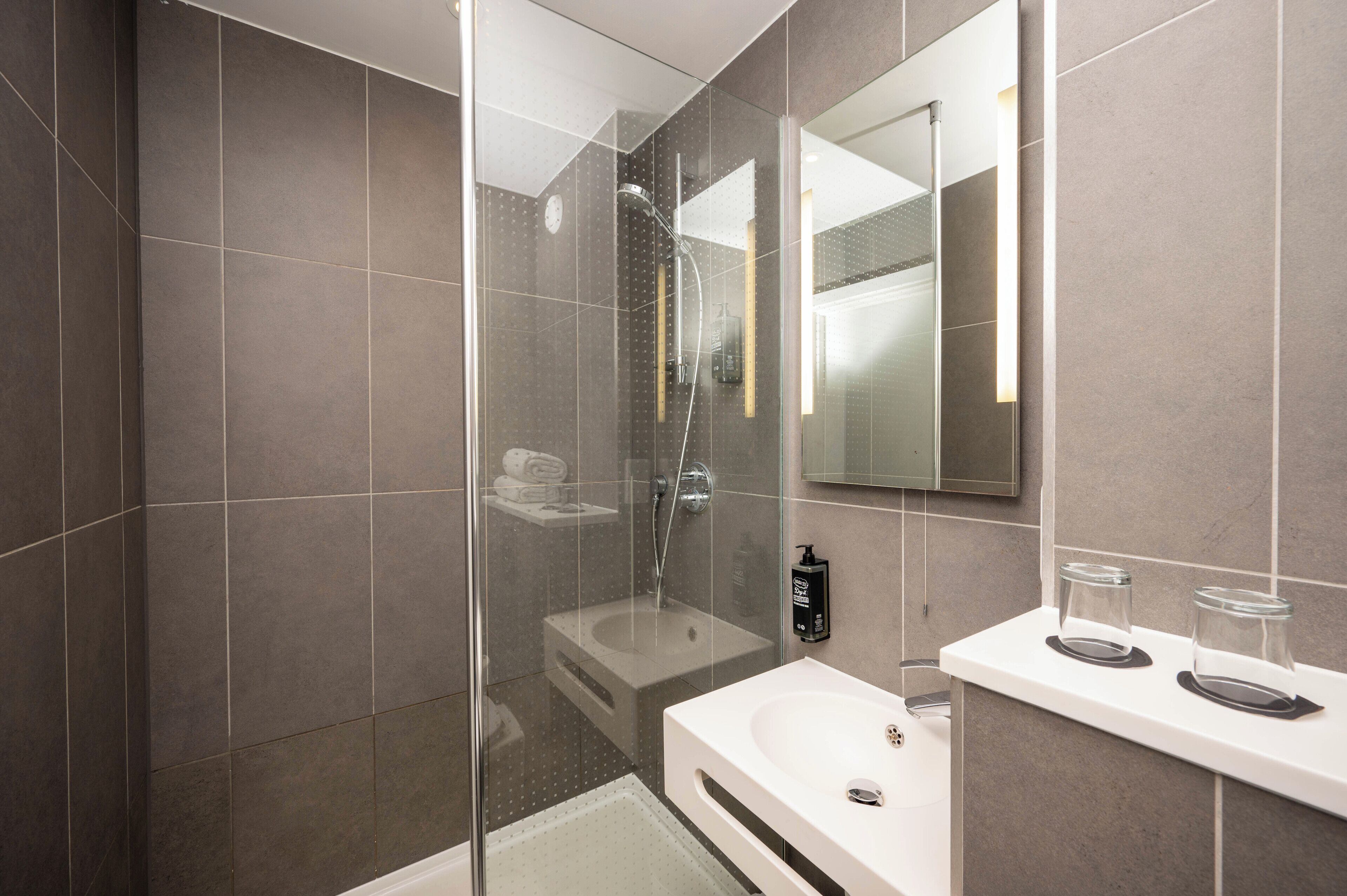 A modern bathroom with a glass-enclosed shower, a white sink, and a large mirror.