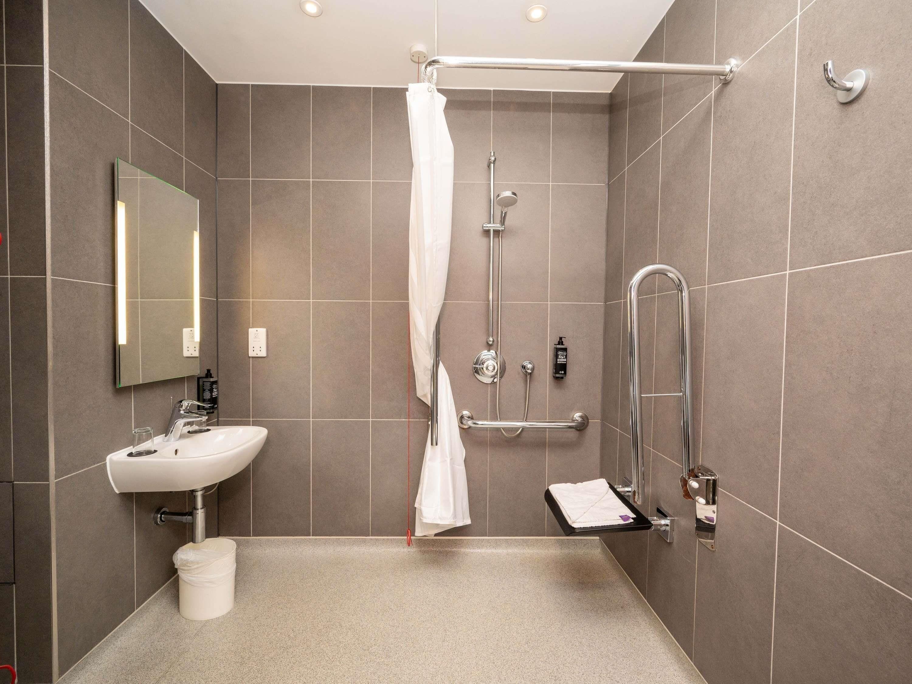 Een moderne badkamer met een douche, wastafel, spiegel en handdoekhouder.