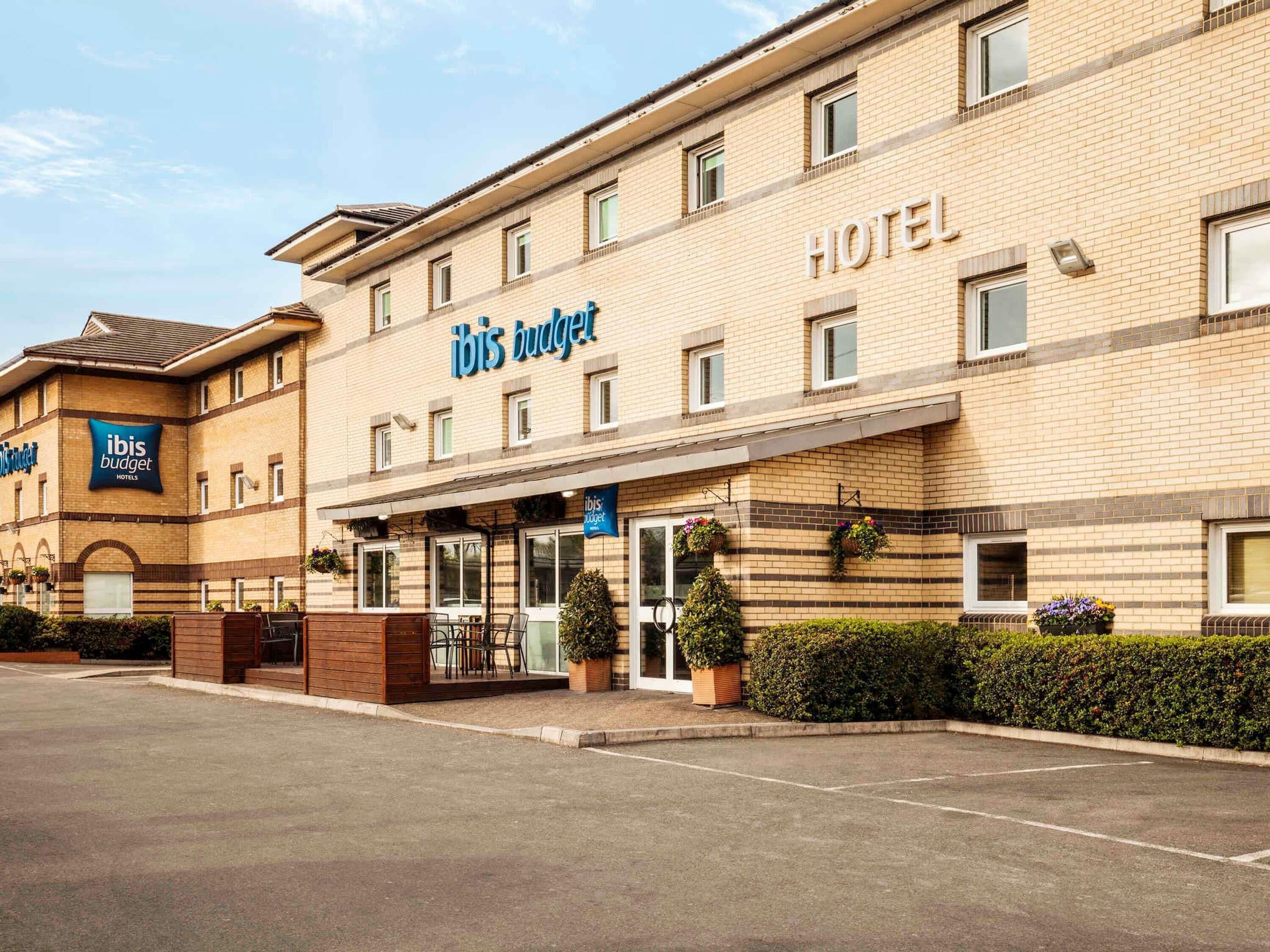 A hotel with a prominent 'ibis budget' sign, a covered entrance, and a parking lot.