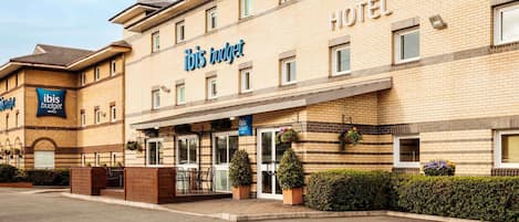Un hotel con un cartel llamativo de 'ibis budget', una entrada cubierta y un estacionamiento.