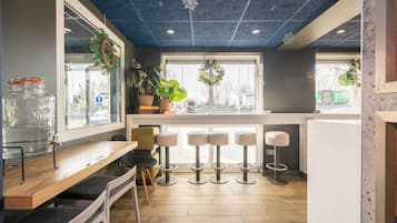 Una zona de bar moderna con mostrador de madera, taburetes y plantas en macetas.