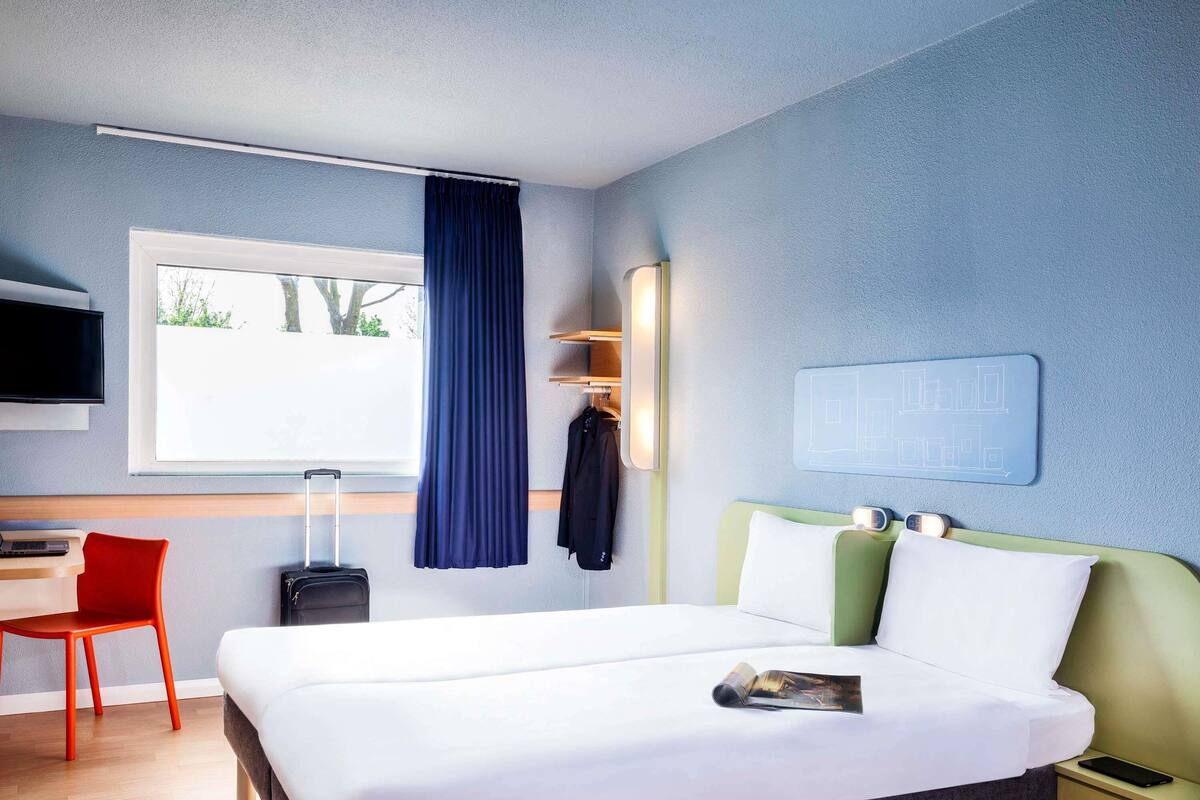 Una habitación de hotel moderna con una cama grande, un escritorio, una silla, un televisor y una ventana con cortina.