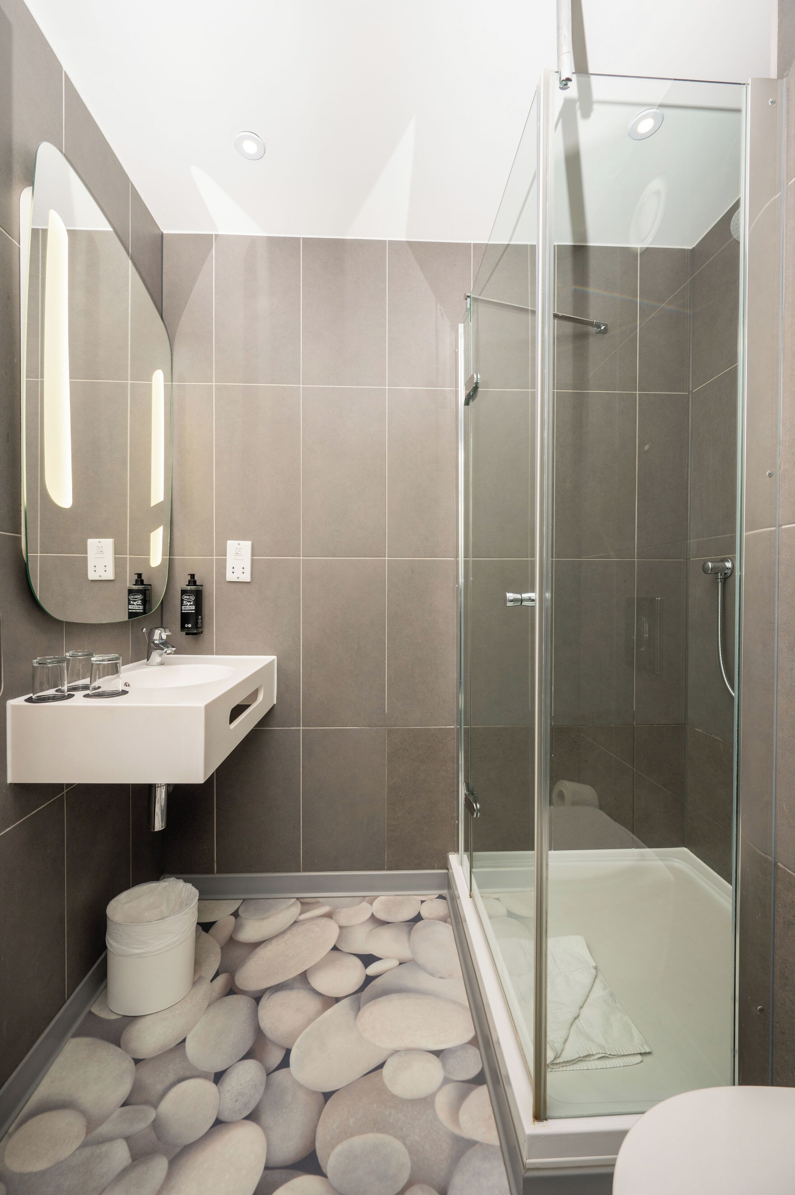 A modern bathroom with a glass-enclosed shower, a white sink, and a large mirror.