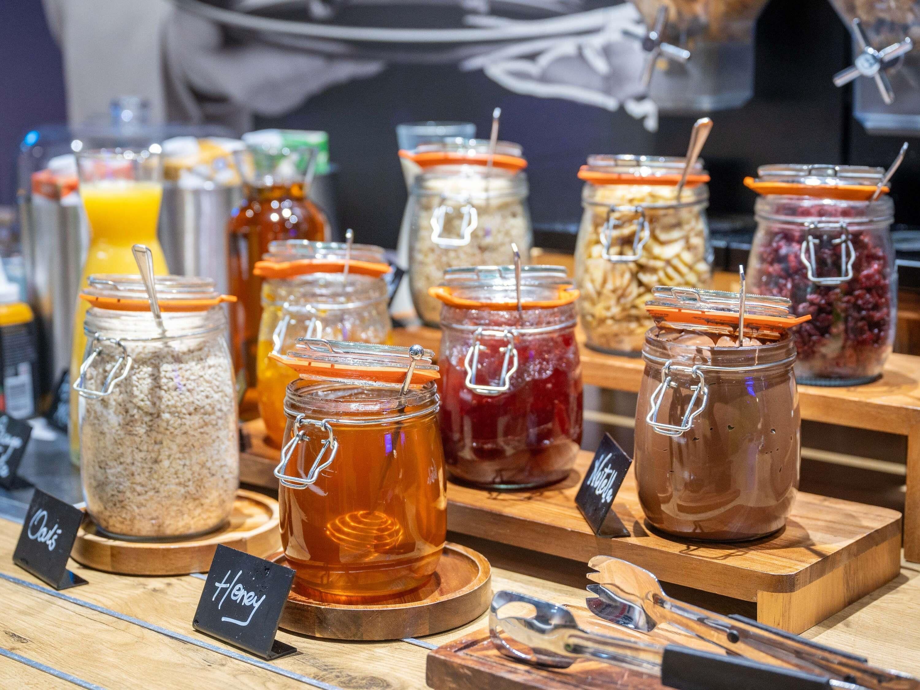 A variety of food items in jars with labels, including honey and chutney, displayed on a wooden counter.