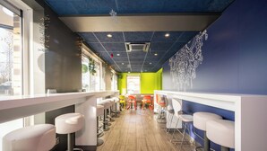 A modern bar area with high stools, a long counter, and a view of the street. - ibis budget London Barking (Barking)