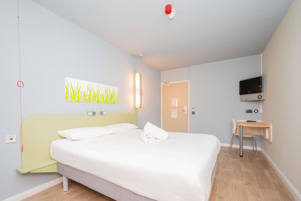 Une chambre d’hôtel avec un lit, un bureau, une télévision et une porte.