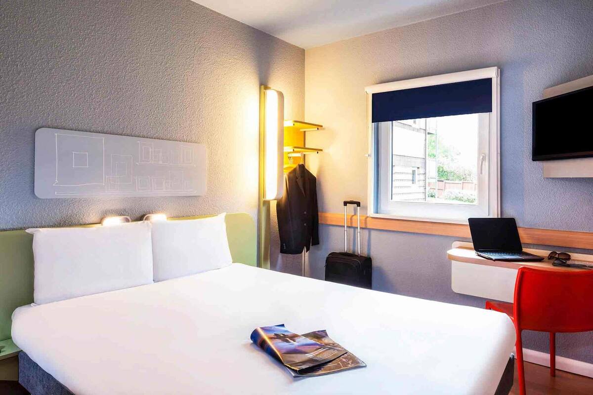 Habitación de hotel con cama, escritorio con laptop, televisión y ventana con vistas.