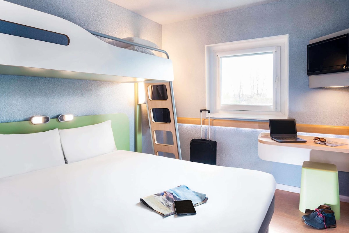 Una habitación de hotel con cama, escritorio, ventana, televisor y escalera.