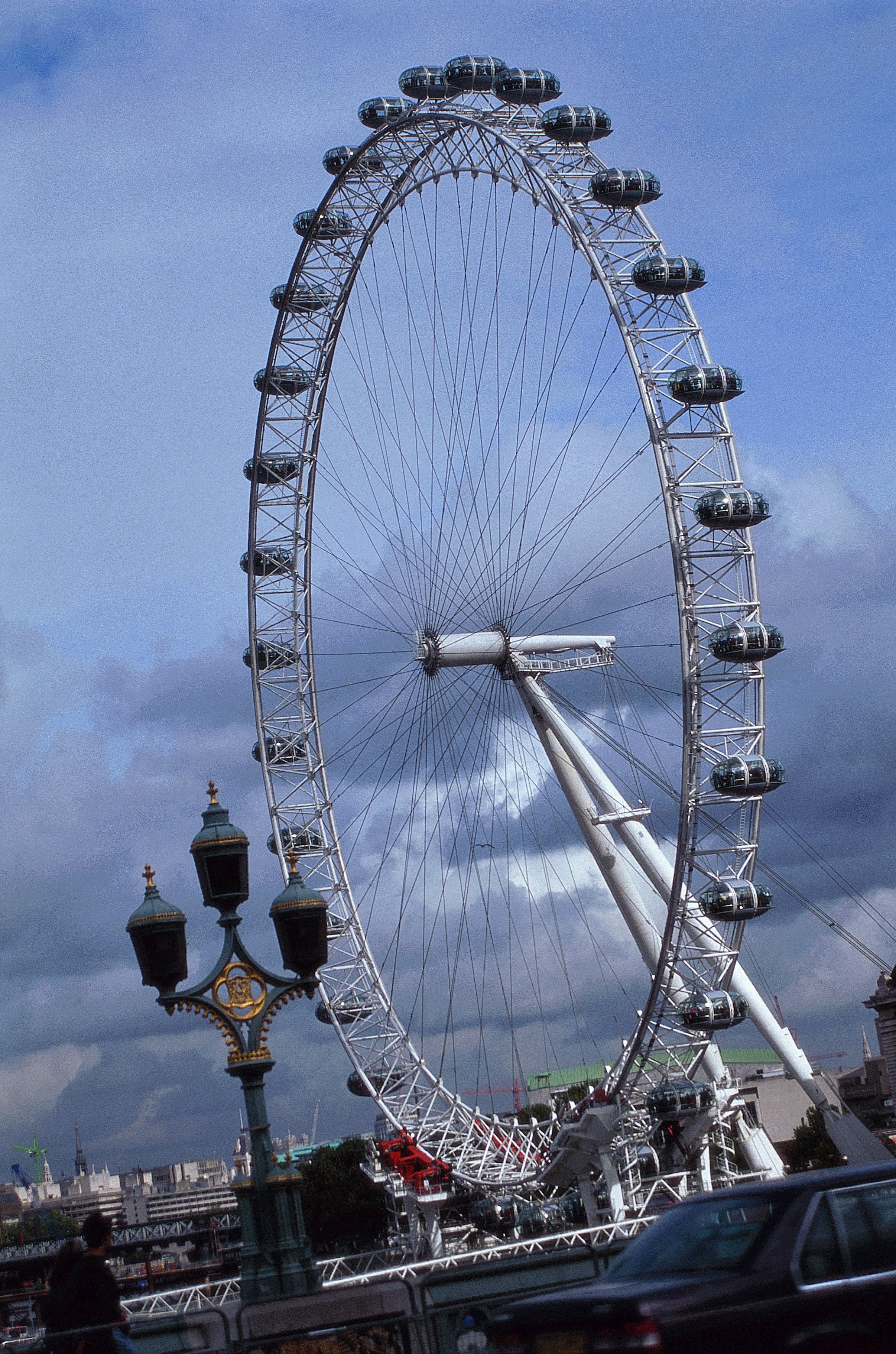 A large Ferris wheel with multiple cabins, a prominent central hub, and a green street lamp with ornate details.