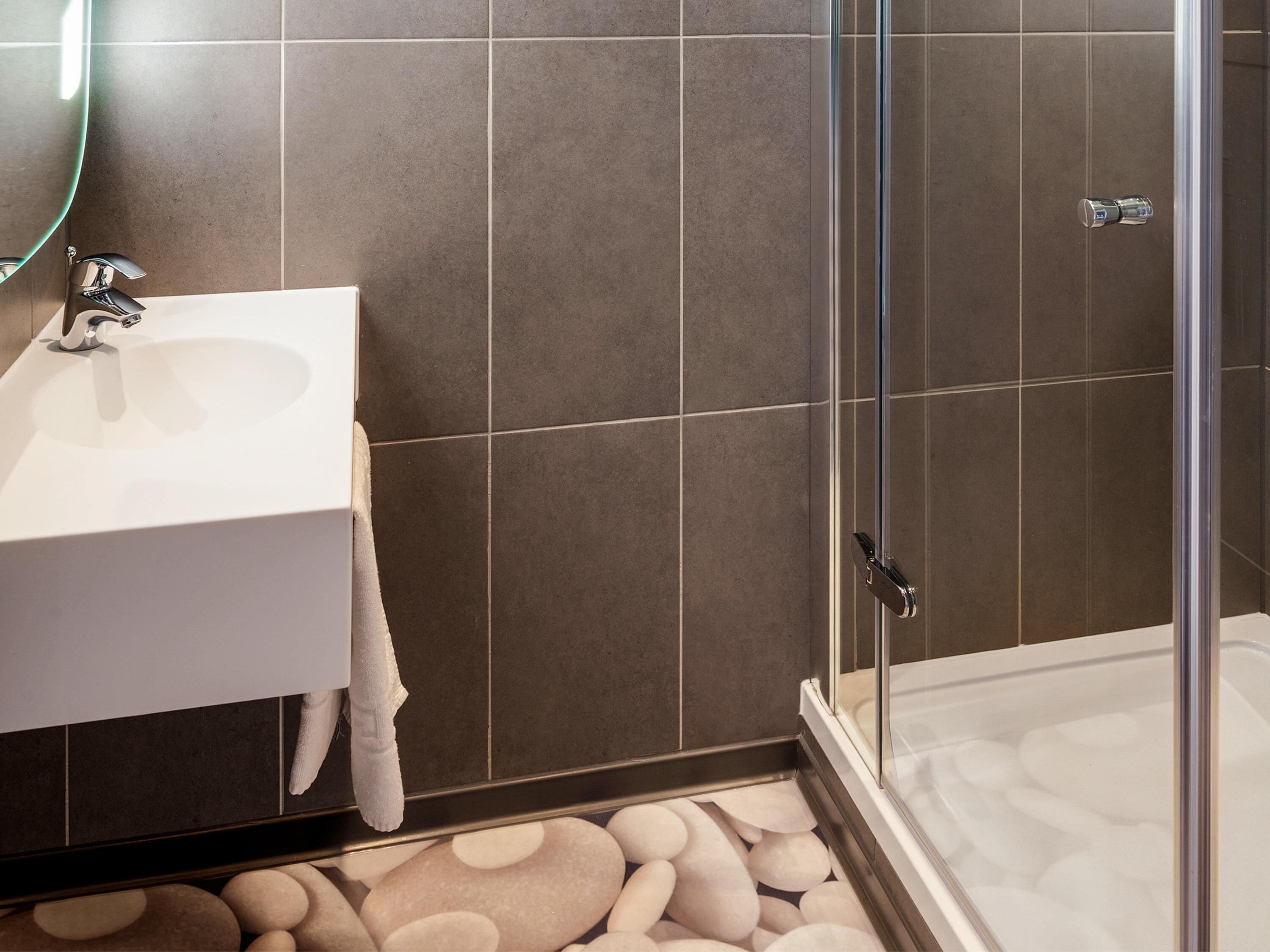 Ein Badezimmer mit einem weißen Waschbecken, einer Duschkabine aus Glas und einem gefliesten Boden.