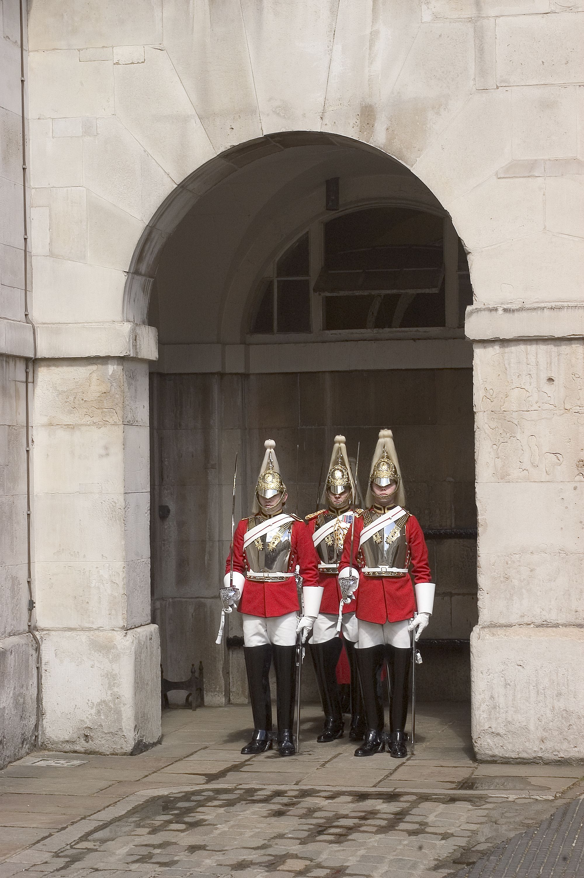 Tres guardias con uniformes rojos de pie frente a un arco de piedra.