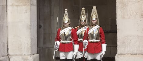 Three guards in red uniforms standing in front of a stone archway.
