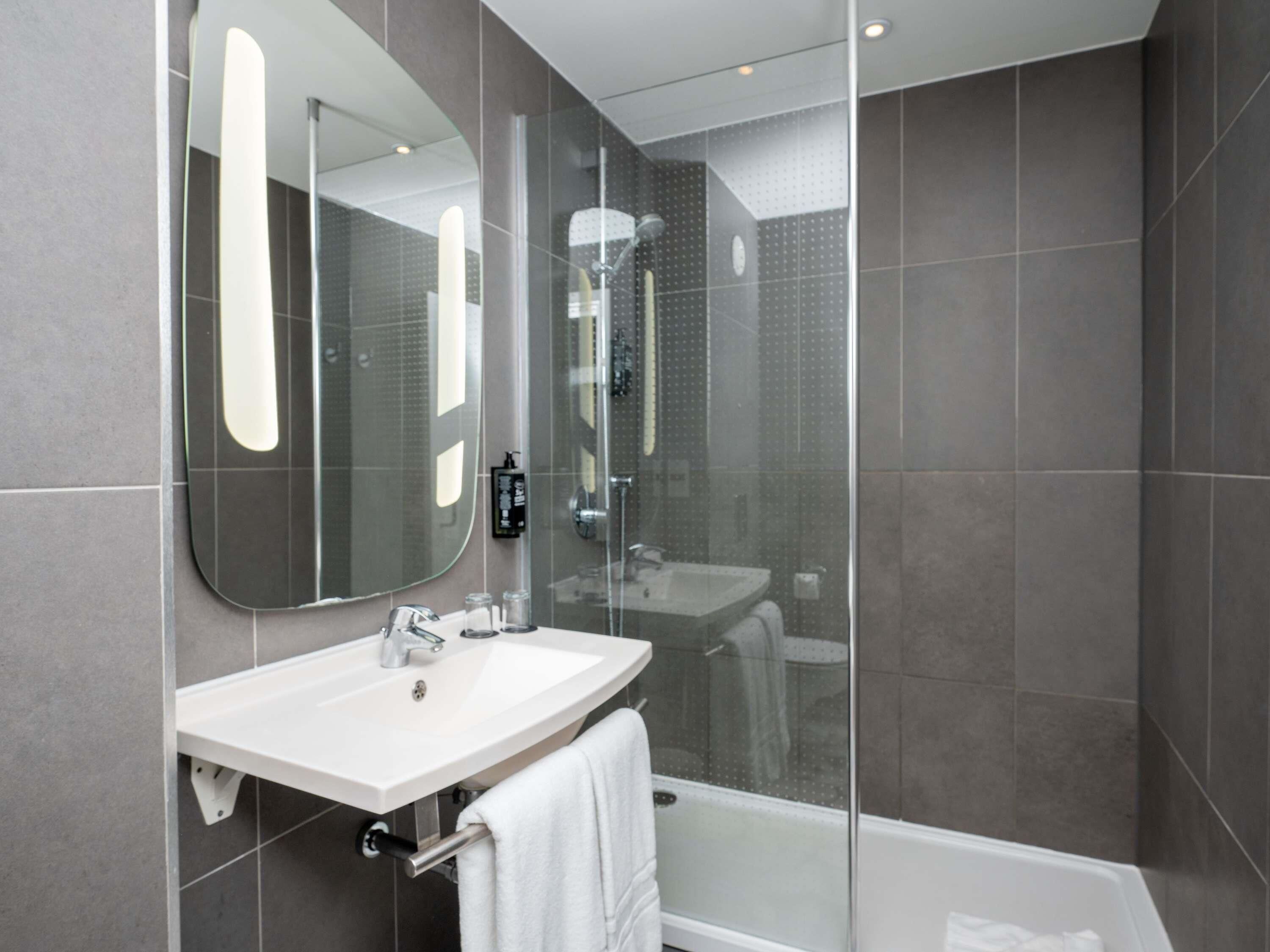A modern bathroom with a glass-enclosed shower, a white sink, and a large mirror.