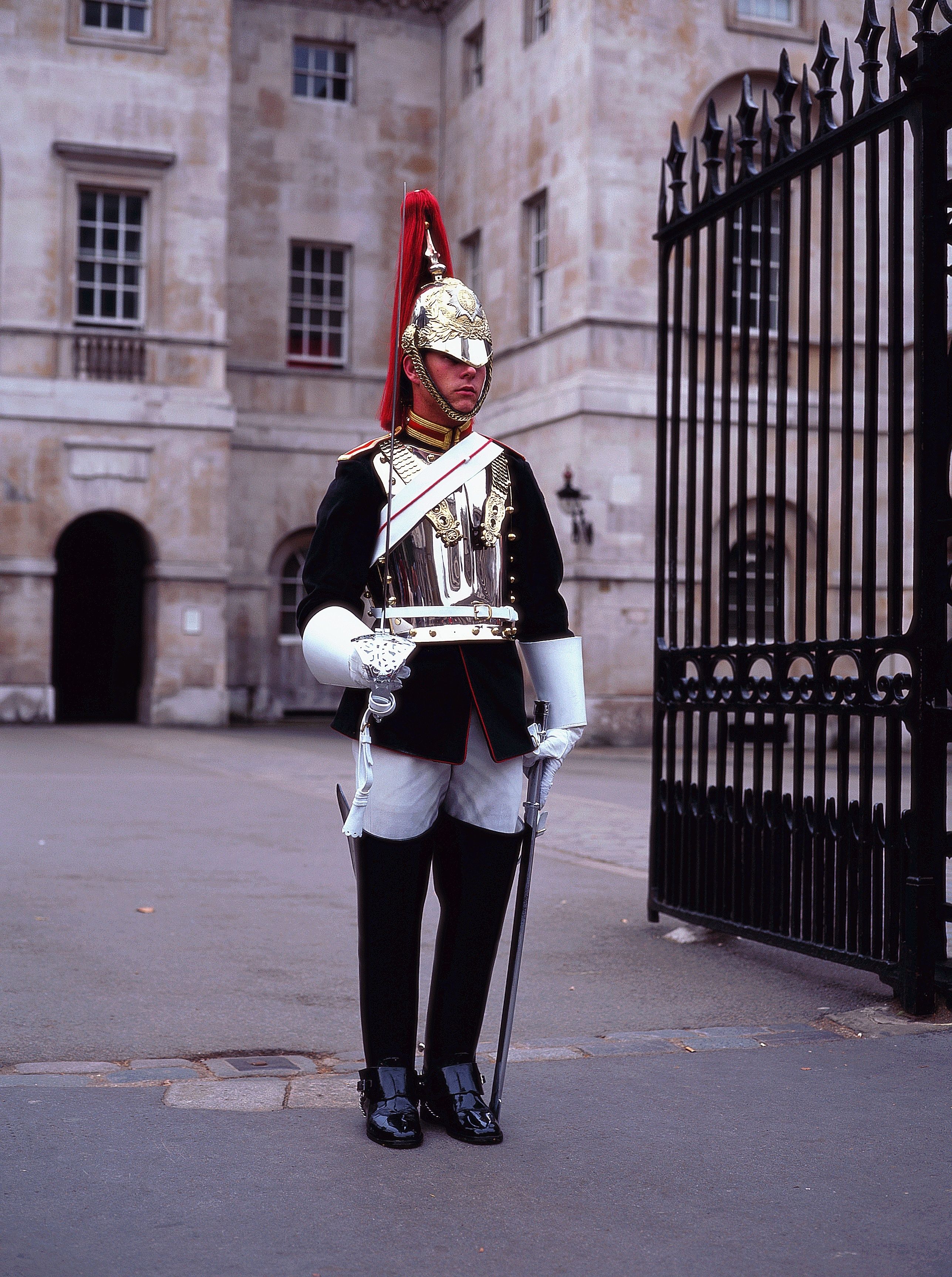 A uniformed guard standing in front of a historic building with a black iron gate.