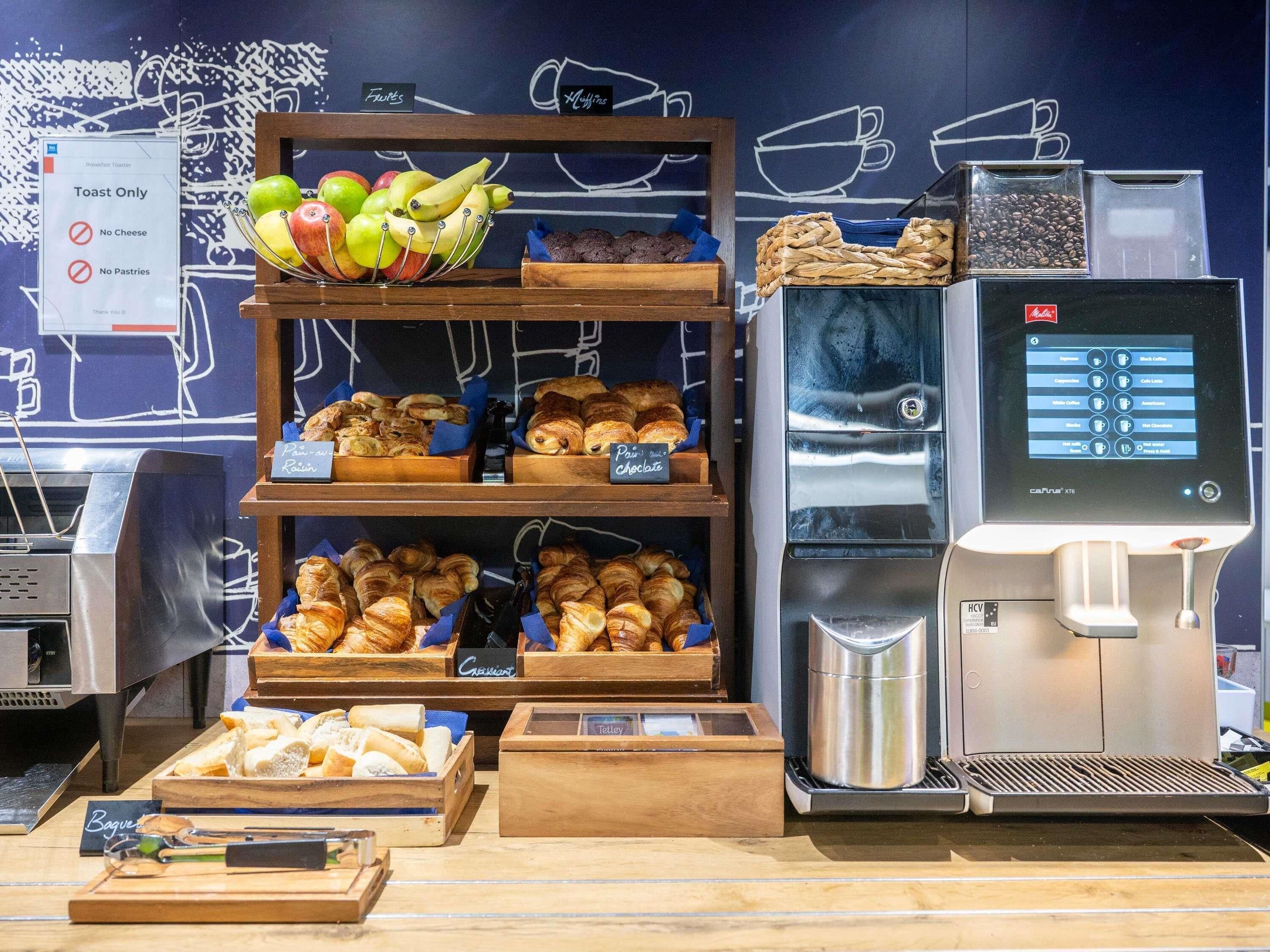 Un buffet de petit-déjeuner avec des fruits, des viennoiseries et une machine à café.