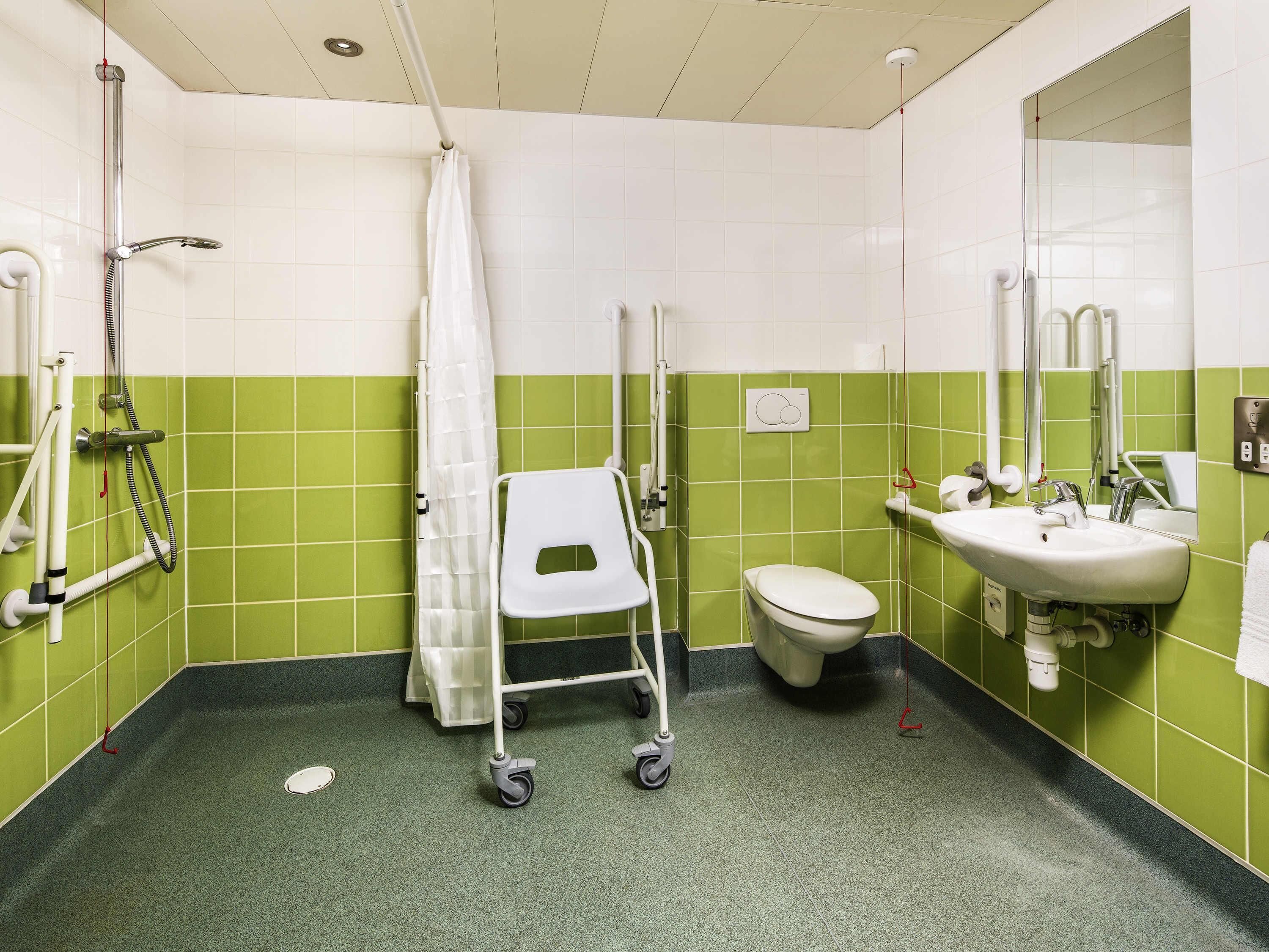 Baño accesible con silla de ruedas, inodoro, lavabo y ducha.