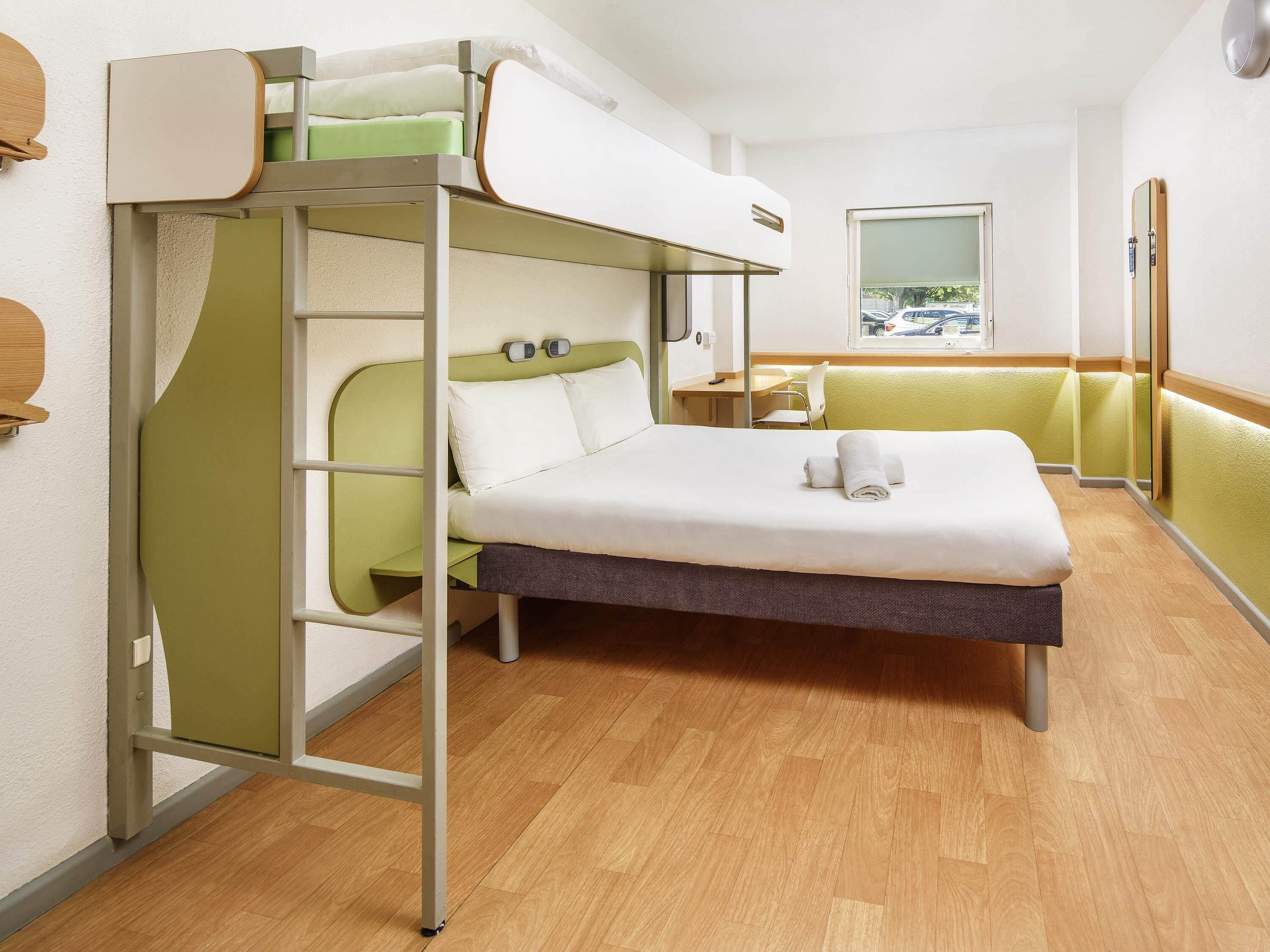 A bunk bed with a desk and chair, a window with a view, and a wooden floor.