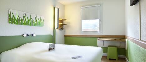 A hotel room with a bed, a small stool, a window, and a green wall.