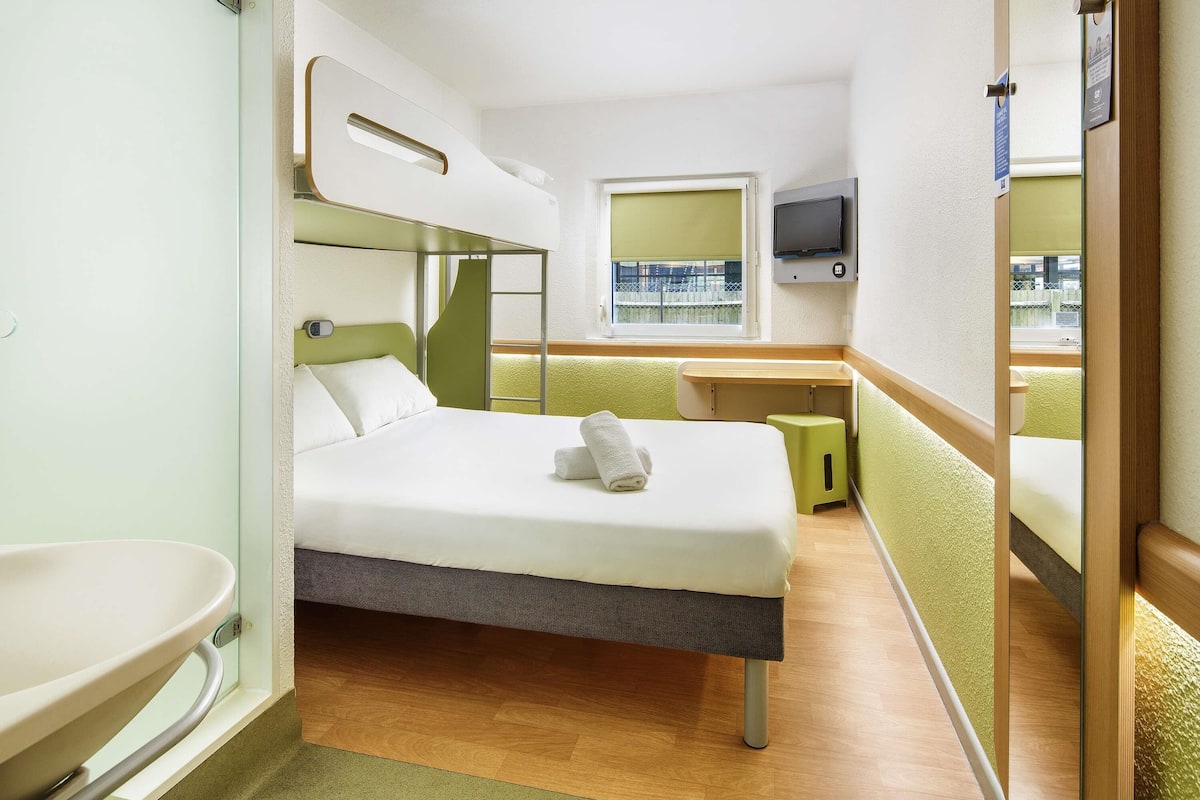 Ein Hotelzimmer mit Bett, Schreibtisch, Fernseher und Fenster.