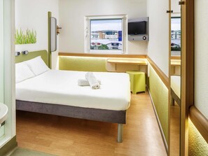 Habitación de hotel con cama, escritorio, televisor, ventana y vista a edificios.