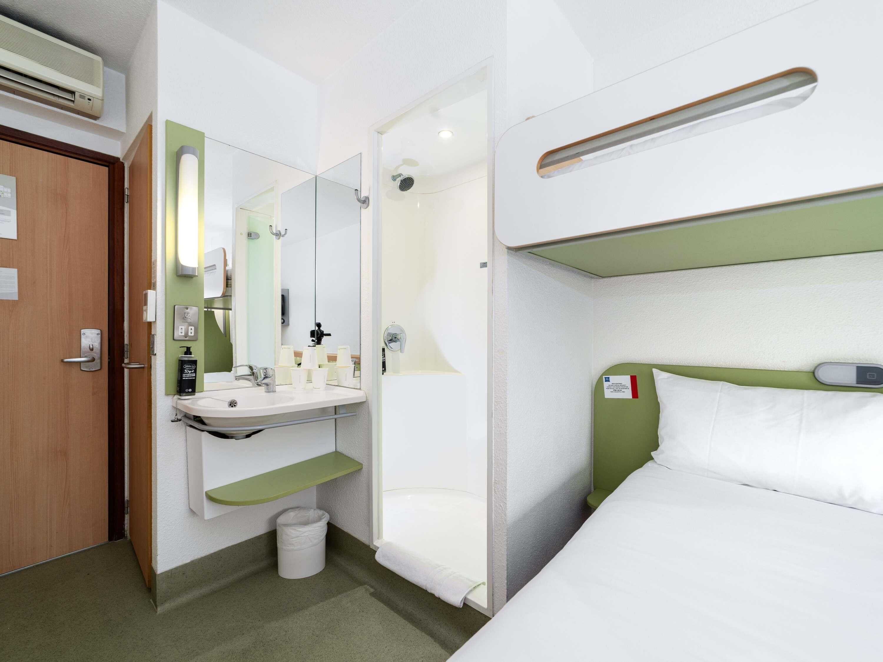 A hotel room with a bed, a bathroom with a sink, mirror, and shower.
