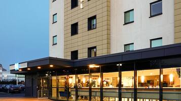 A hotel with a modern facade, large windows, and a visible restaurant area with outdoor seating.