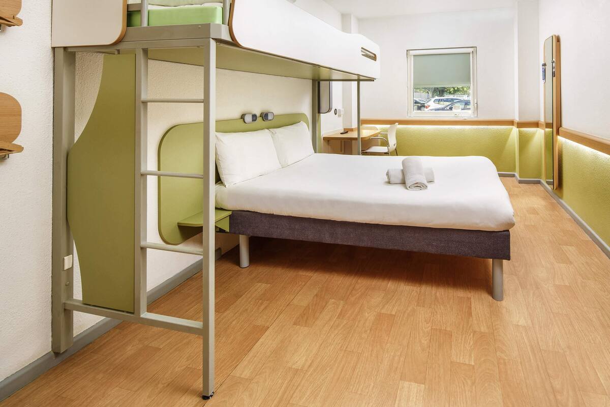 A bunk bed with a desk and chair, a window with a view, and a wooden floor.